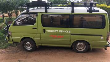 A green tourist vehicle parked on a dirt road with trees in the background.