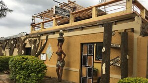 Un bâtiment doté d’une façade originale, ornée de structures évoquant des arbres et d’une statue représentant une personne portant un pot. Une enseigne indique la présence d’un café et d’un restaurant.