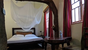 Une chambre à coucher avec un lit sous un dais, une table en bois avec une bouteille d’eau et une chaise.