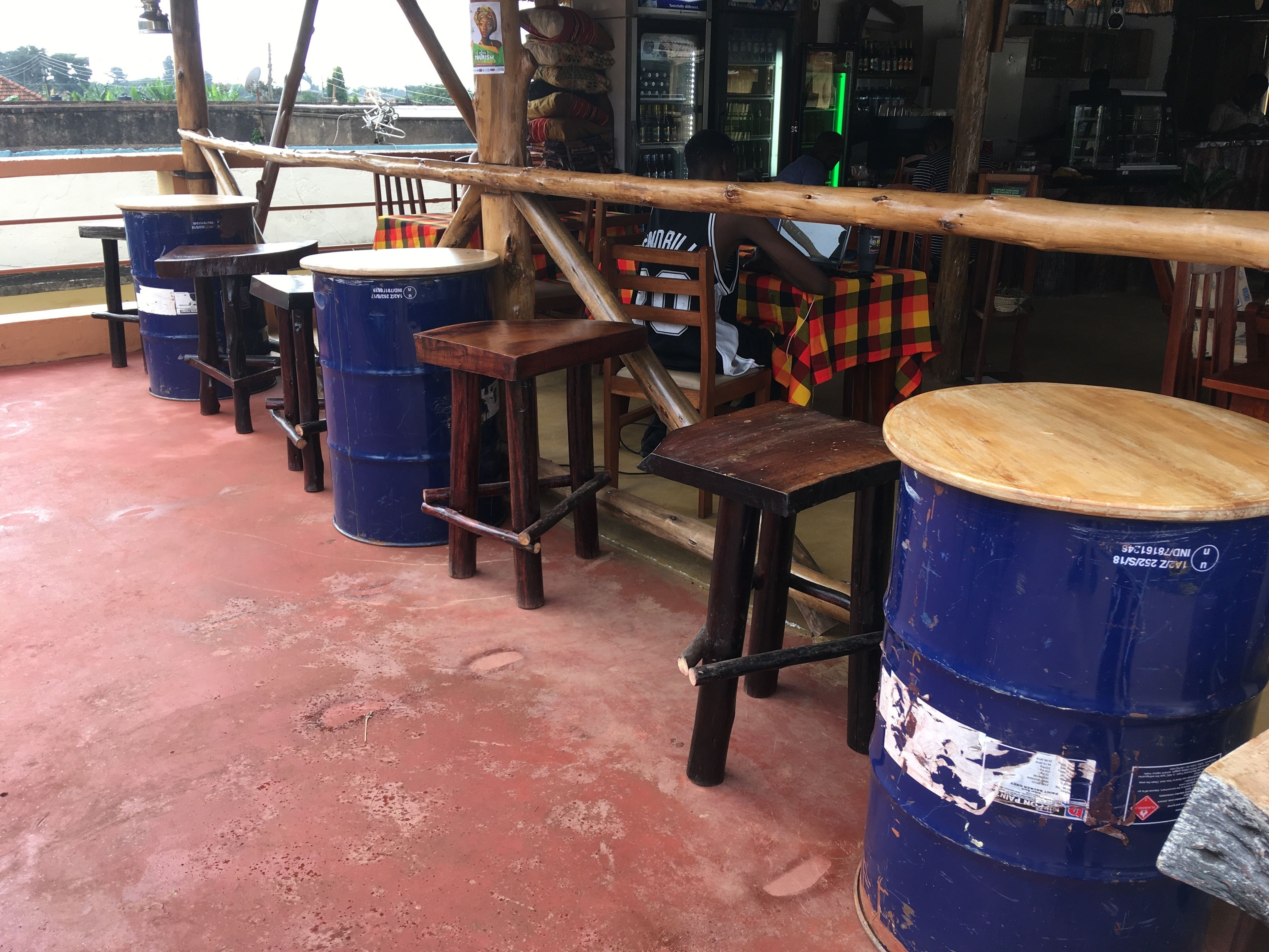 A bar area with wooden stools and blue barrels, a wooden bar counter, and a view of the street outside.