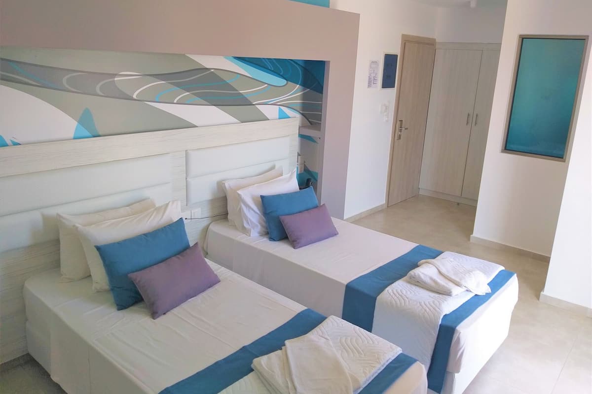 Habitación de hotel con dos camas, cada una con una colcha azul y blanca, y un cuadro abstracto grande sobre las camas.