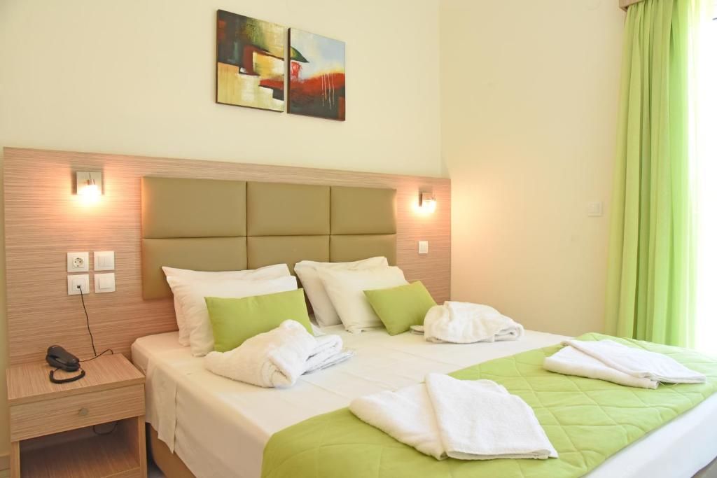 A hotel room with a bed, green pillows, white towels, a headboard, a nightstand, a phone, and a painting on the wall.