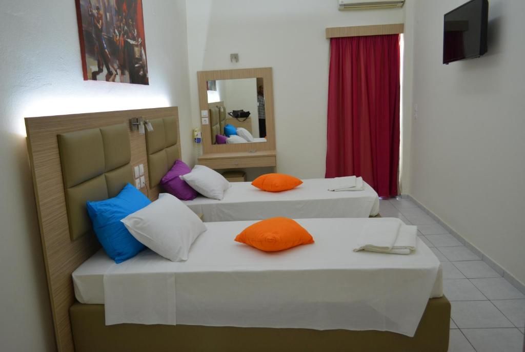 A hotel room with two beds, a mirror, a television, and a red curtain.
