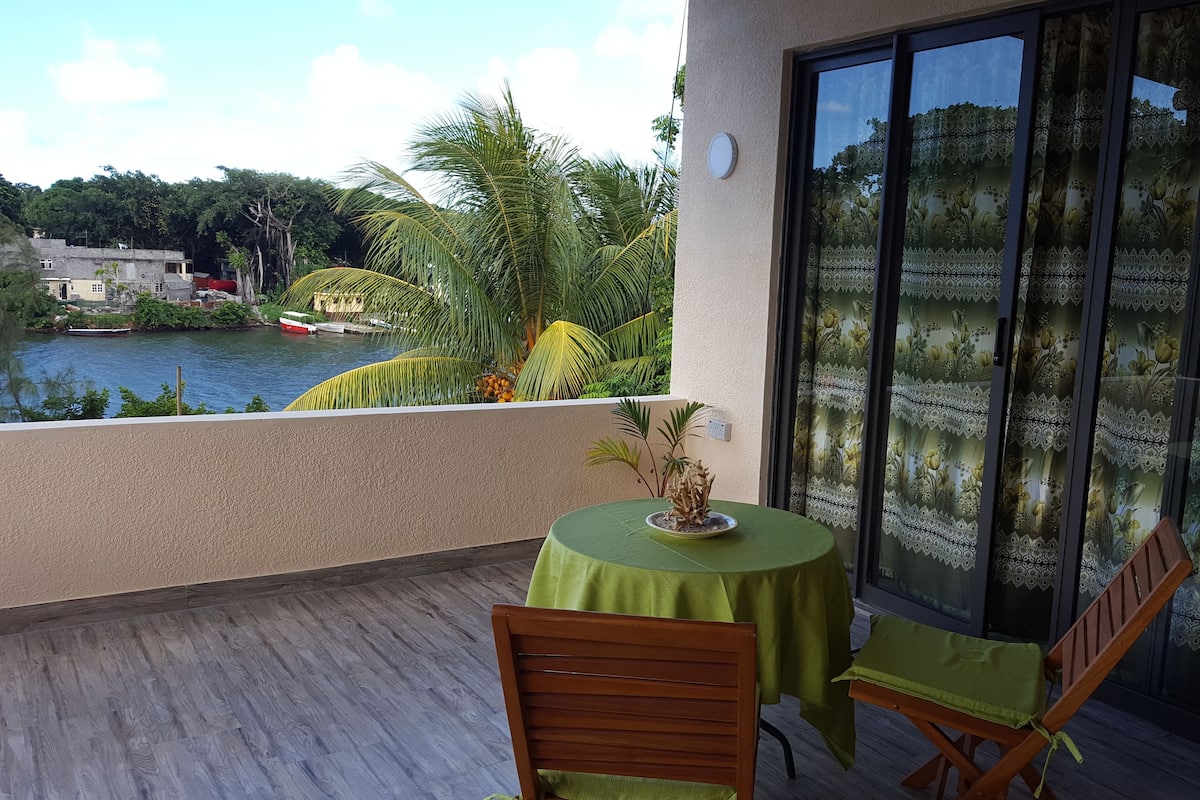 A balcony with a table and chairs, overlooking a river and greenery.