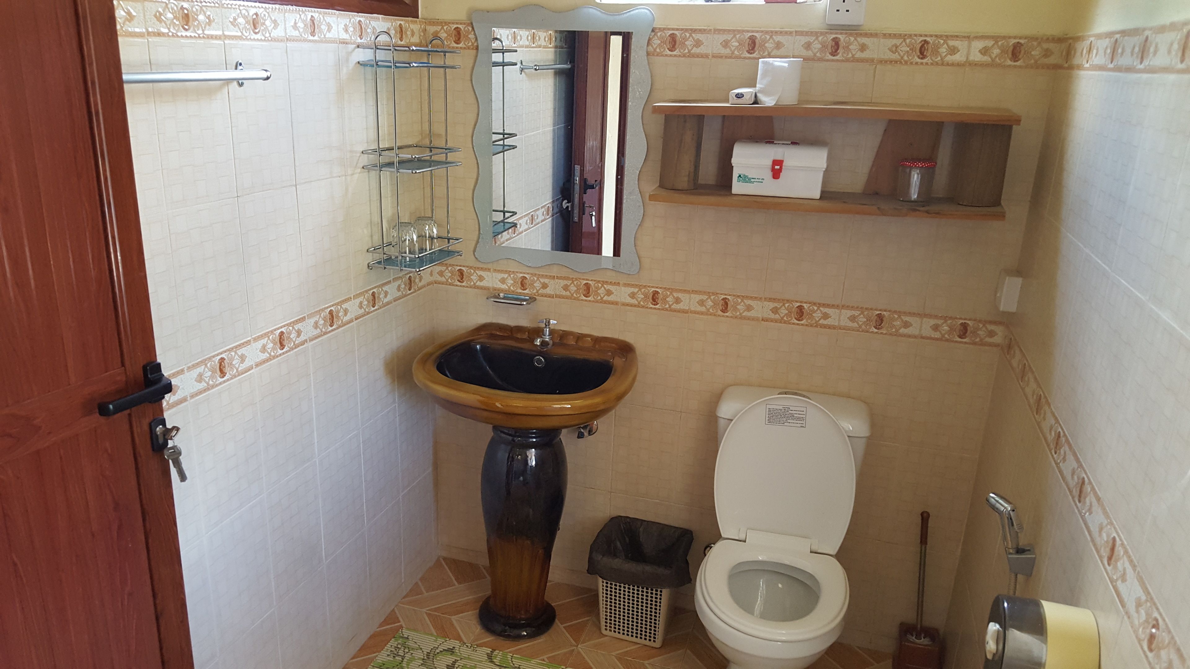 Uma casa de banho com lavatório de madeira, sanita, espelho e prateleira com artigos de higiene pessoal.