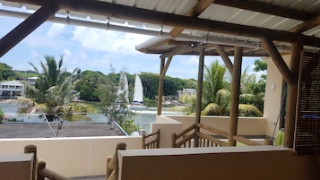 Un espacio al aire libre techado con vistas a un cuerpo de agua, palmeras y un velero.