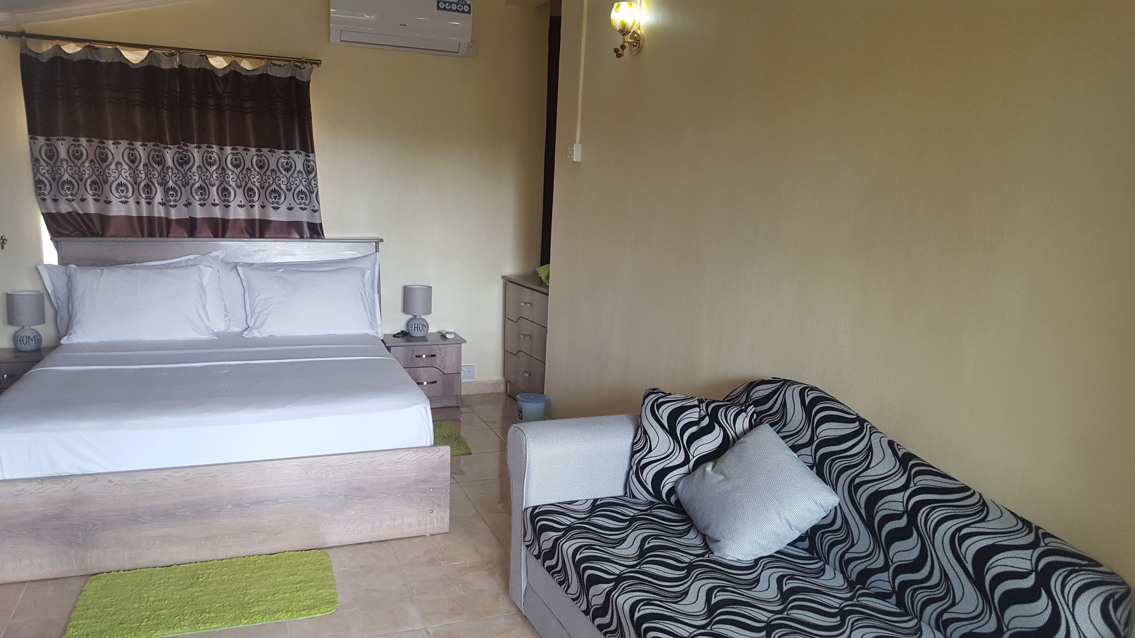 Un dormitorio con cama, mesita de noche, lámpara y sofá.