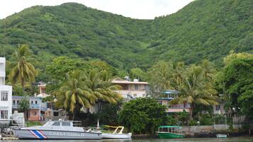 Uma área costeira com um barco da Guarda Costeira atracado perto de edifícios e palmeiras, com uma montanha ao fundo.
