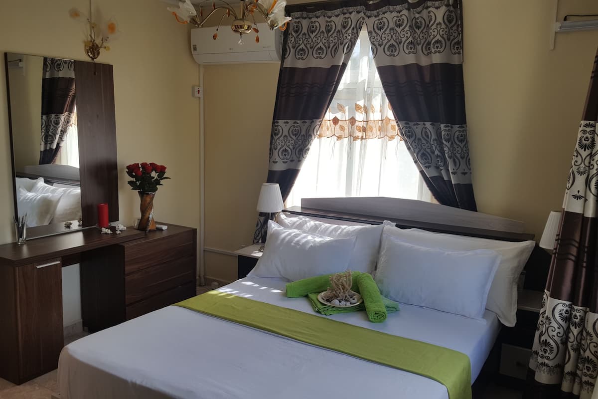 A hotel room with a bed, a dresser, a mirror, a vase with flowers, and patterned curtains.