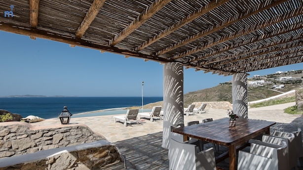A wooden pergola with a view of the sea, stone walls, and a table with chairs. - Anerousses Mykonian Traditional Houses (Mykonos)