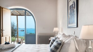 A bedroom with a large bed, a view of the sea, and a door leading to an outdoor area. - Anerousses Mykonian Traditional Houses (Mykonos)