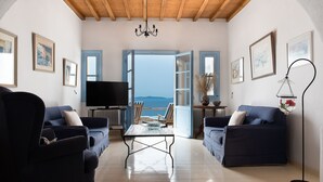 A living room with two dark blue sofas, a coffee table, and a TV. There are framed pictures on the walls and a chandelier. - Anerousses Mykonian Traditional Houses (Mykonos)