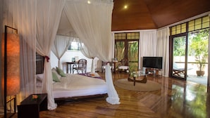 A spacious room with a large bed, wooden flooring, a TV, and a dining area. - Mandala Spa and Resort Villas (Boracay Island)