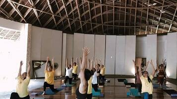 A yoga class in a room with a high wooden ceiling and a large mirror on the wall.