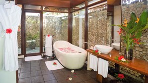 A bathroom with a bathtub, a sink, and a mirror. There are towels and a robe hanging on the wall. - Mandala Spa and Resort Villas (Boracay Island)