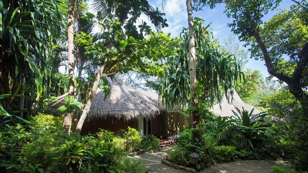 A thatched-roof hut surrounded by lush greenery and a cobblestone path. - Mandala Spa and Resort Villas (Boracay Island)