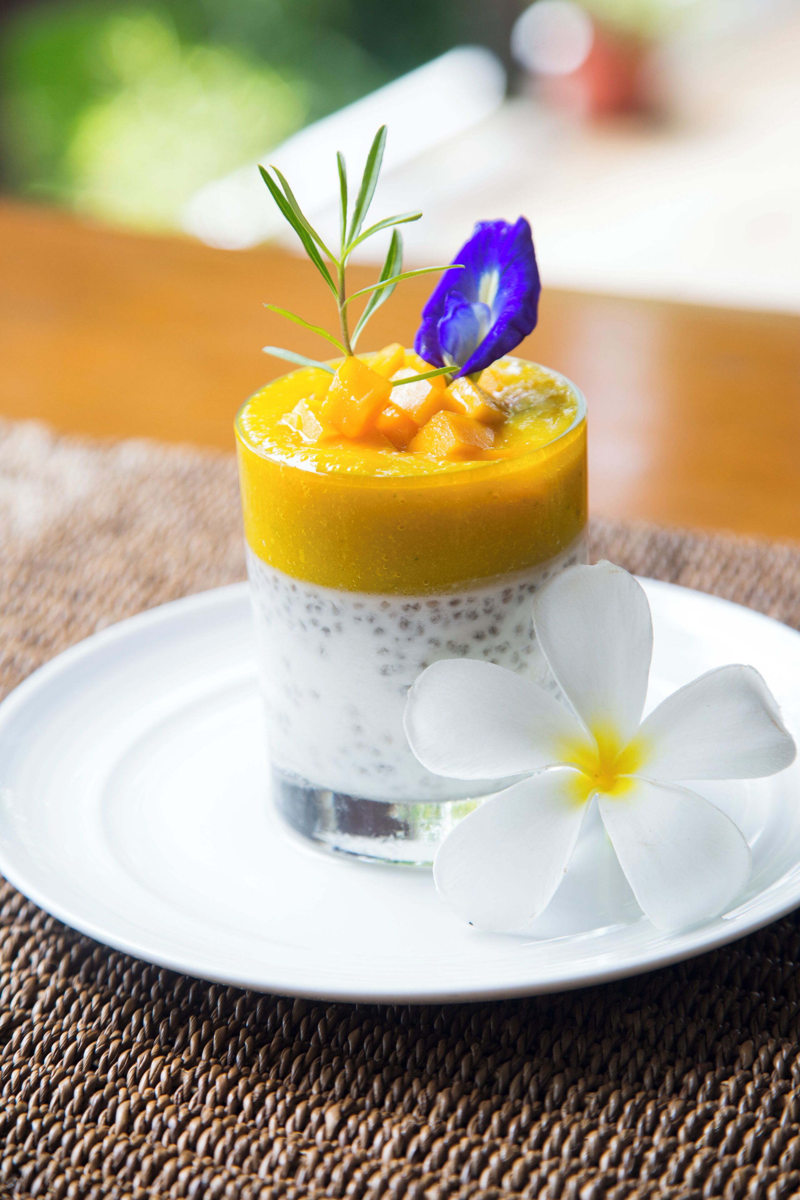 Un postre en un vaso con una flor blanca sobre un plato.