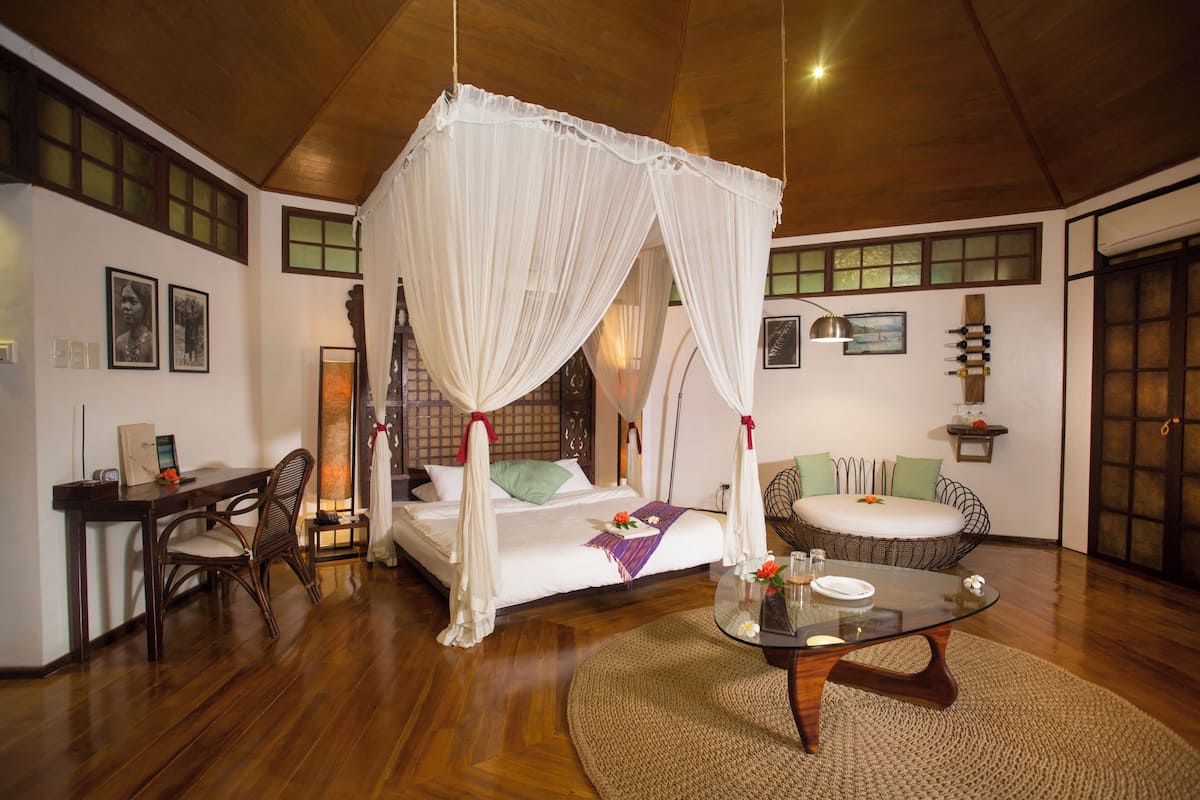 A room with a four-poster bed, a sitting area with a sofa and a coffee table, a wooden desk, and a chair.