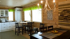 Interior de una cabaña de madera con comedor, cocina y una araña.