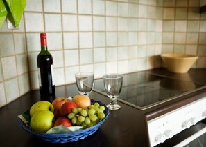 Una encimera de cocina con una cesta de frutas que contiene manzanas y uvas, una botella de vino y dos copas de vino vacías.
