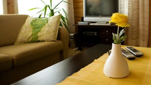 Un salón con un sofá, televisión, una planta y un florero con una flor sobre una mesa.