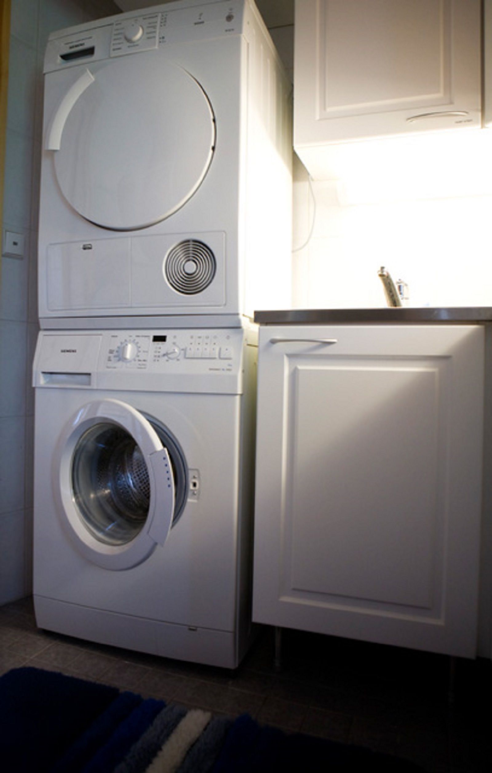A stacked washer and dryer unit in a laundry room with a cabinet above.