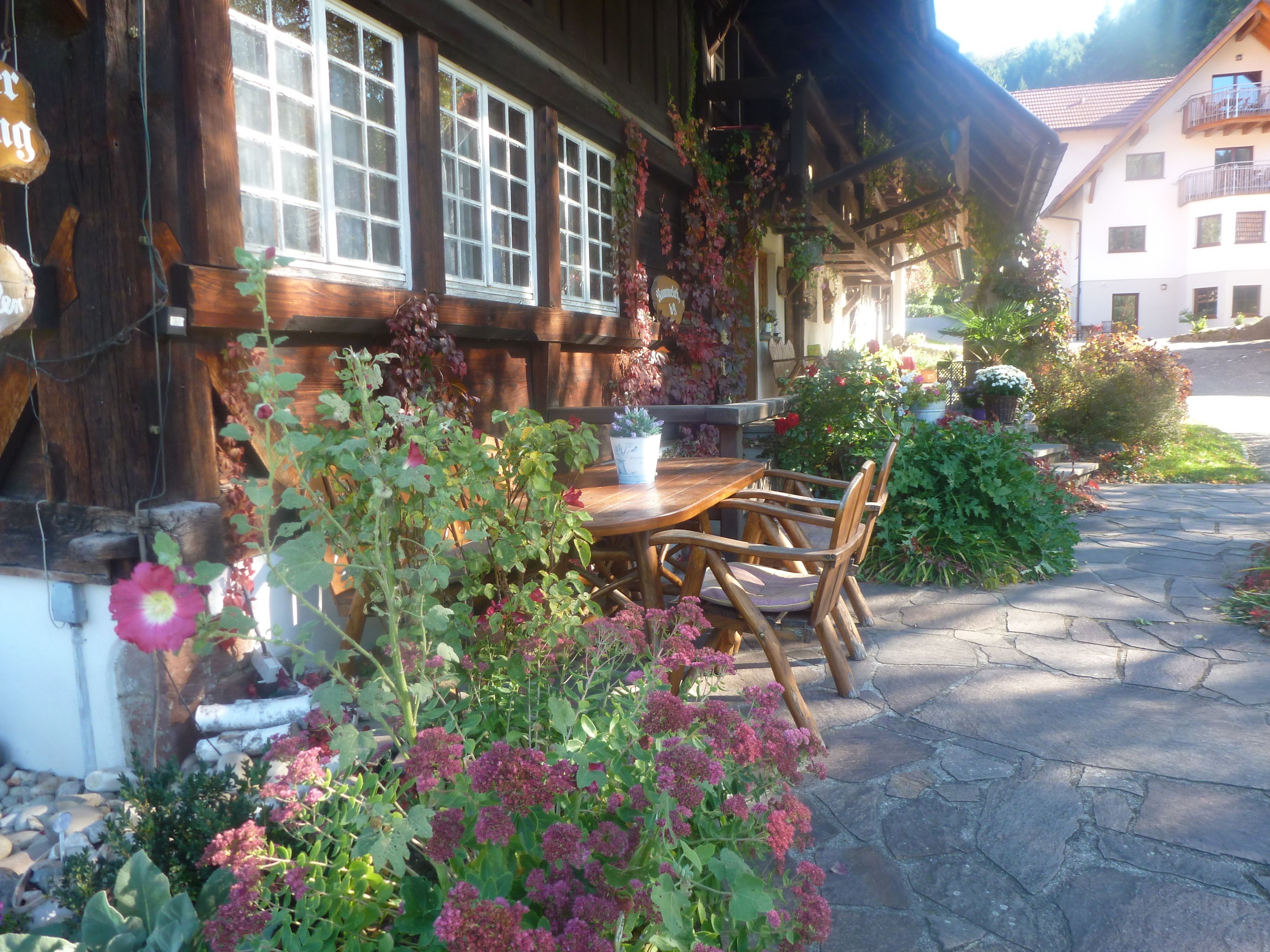 Un bâtiment en bois doté de grandes fenêtres, d’une entrée pavée de pierres et d’une table avec des chaises à l’extérieur.