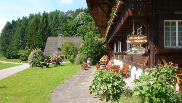 A rustic wooden building with a stone pathway leading to a seating area. - Rommelehof (Gutach)