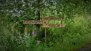 A wooden directional signpost surrounded by lush greenery. - Salkolahti Vehmaanpirtti (Orivesi)