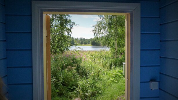 A view through a doorway into a natural landscape with a lake and dense vegetation. - Salkolahti Vehmaanpirtti (Orivesi)