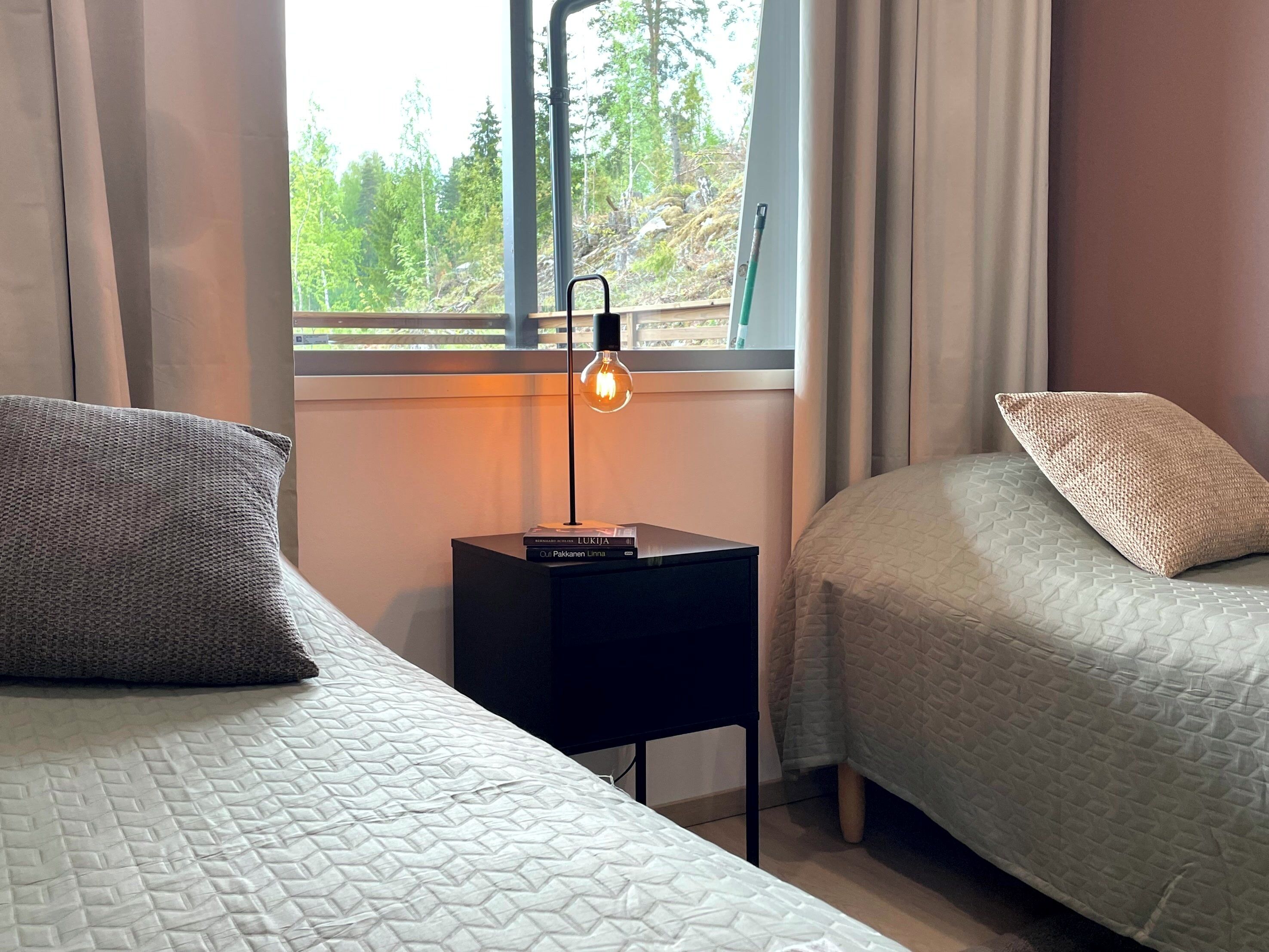 Un dormitorio con dos camas, una mesita de noche con una lámpara y una ventana con vista a árboles.