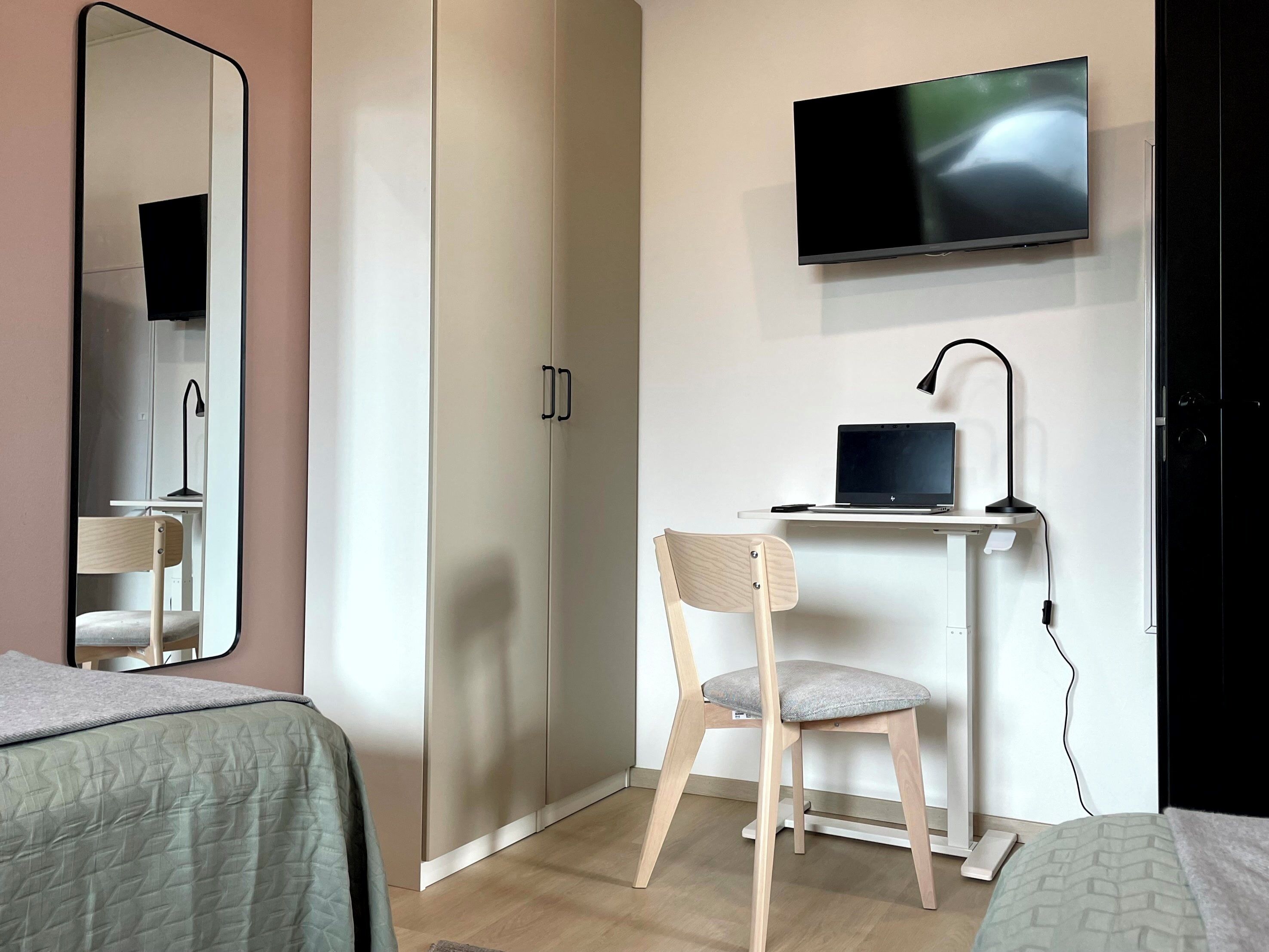 Un dormitorio con una cama, un escritorio con una computadora portátil, una silla, un televisor y un armario.