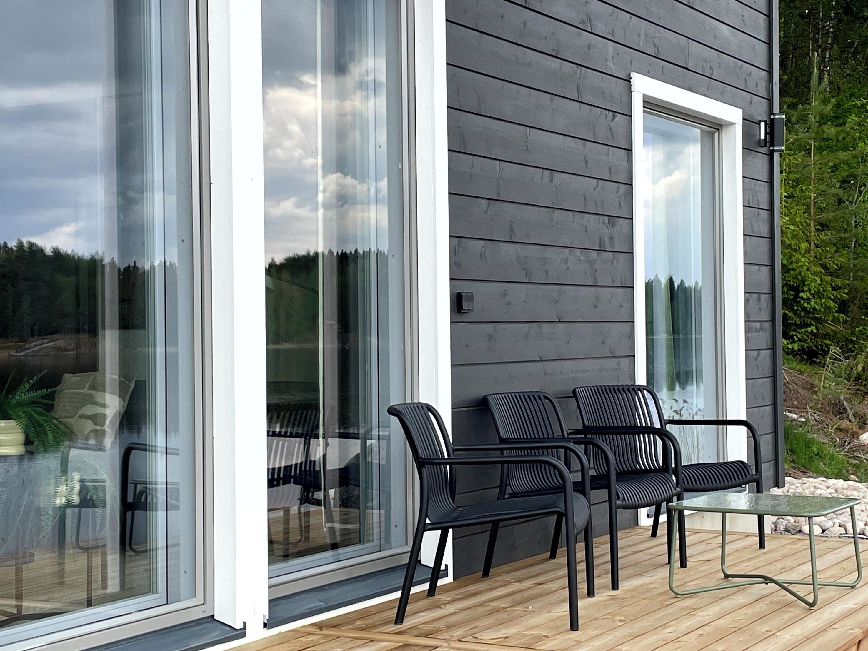A modern outdoor seating area with a glass door leading to a deck, surrounded by dark wooden walls.