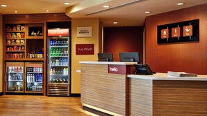 Un espace d’accueil d’hôtel avec un comptoir de réception en bois, un minibar et un réfrigérateur rempli de boissons et d’en-cas.