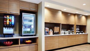 Un espace moderne en libre-service où l’on peut prendre son petit-déjeuner, avec un distributeur de boissons réfrigéré, une variété de boissons et un choix de fruits et de viennoiseries.