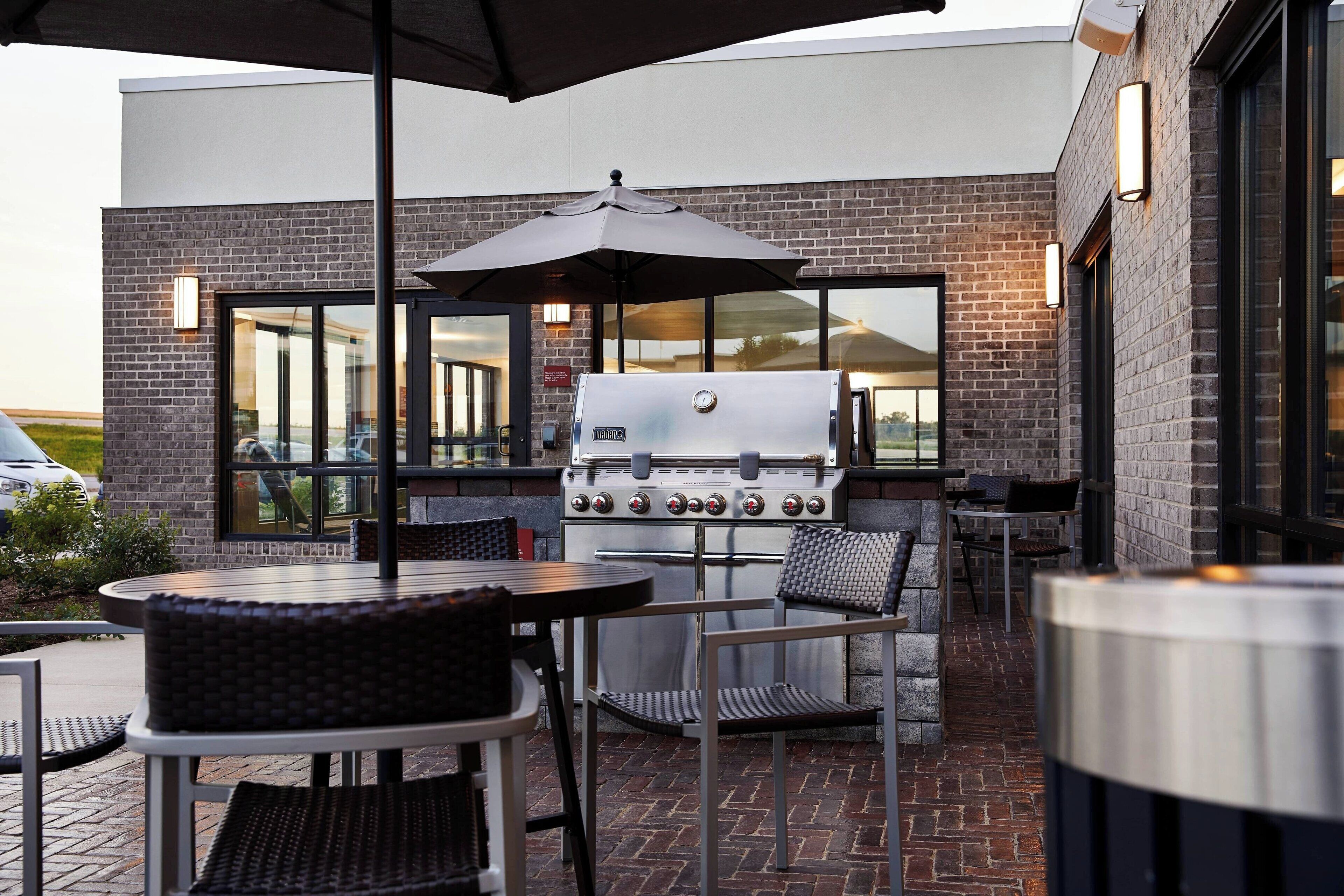 Un patio exterior con una parrilla, mesas y sillas.