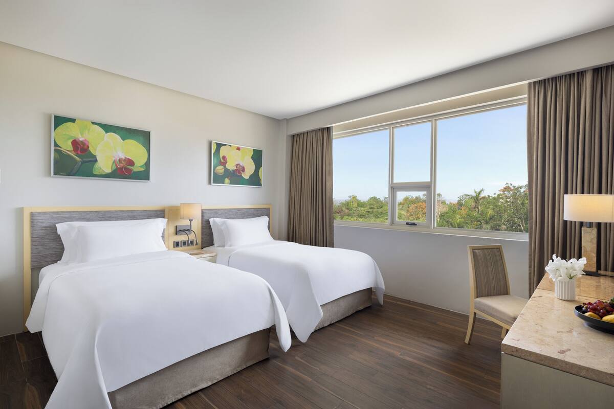 Ein Hotelzimmer mit zwei Betten, einem Schreibtisch, einem Stuhl und einem großen Fenster mit Vorhängen.