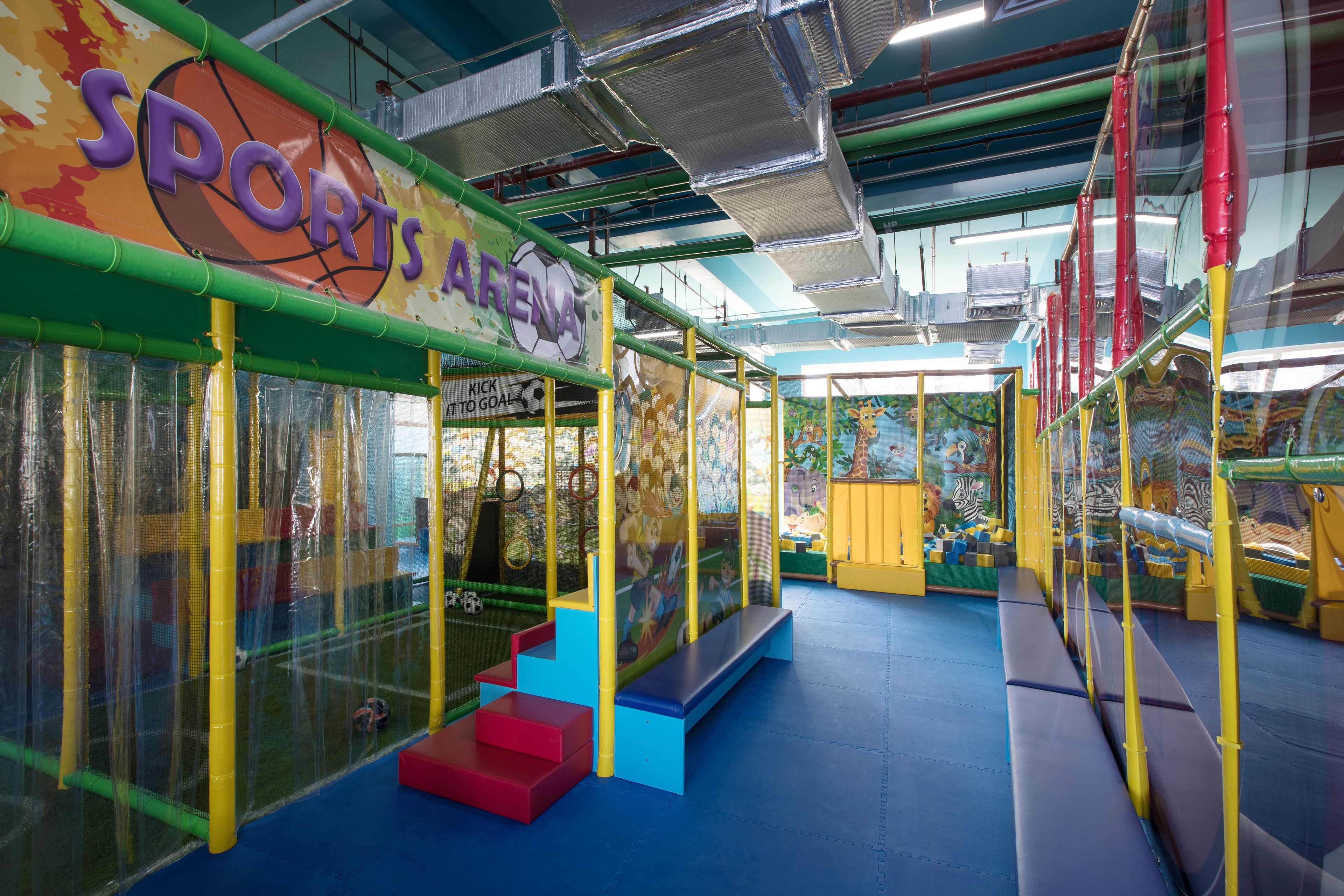 Egy fedett játszótér, színes játékfelszerelésekkel és egy „SPORTS ARENA” felirattal.