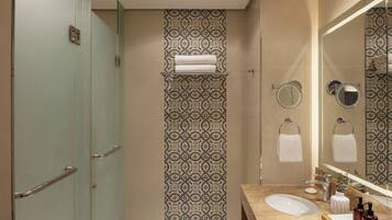 A modern bathroom with a glass shower enclosure, patterned wall tiles, a vanity with a sink, and a large mirror.