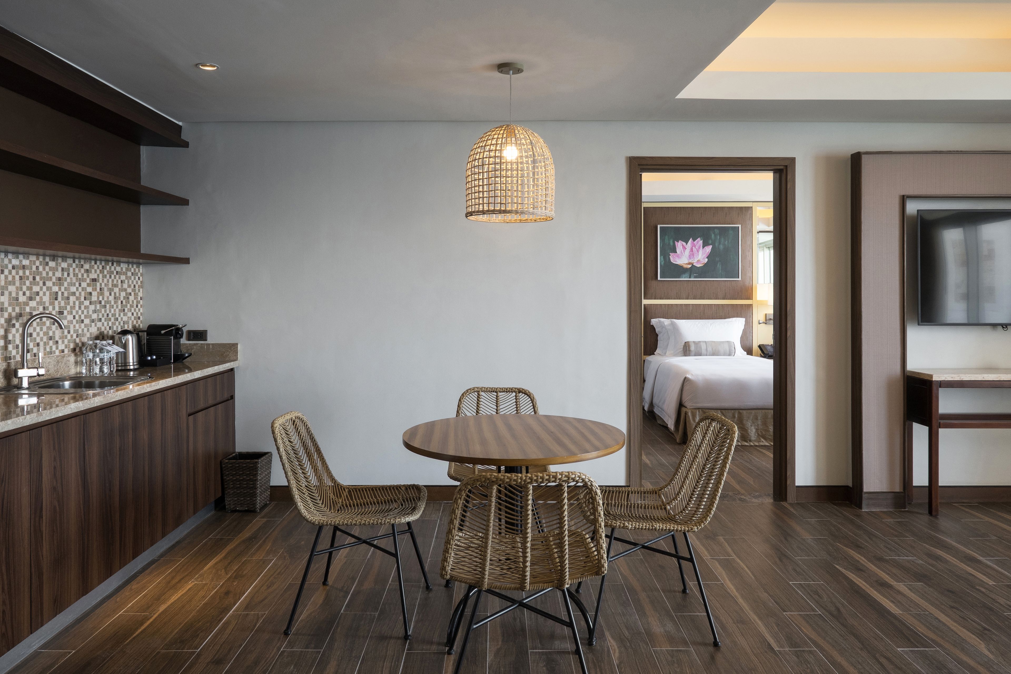 A modern kitchen with a dining area, a TV, and a bedroom visible through an open door.