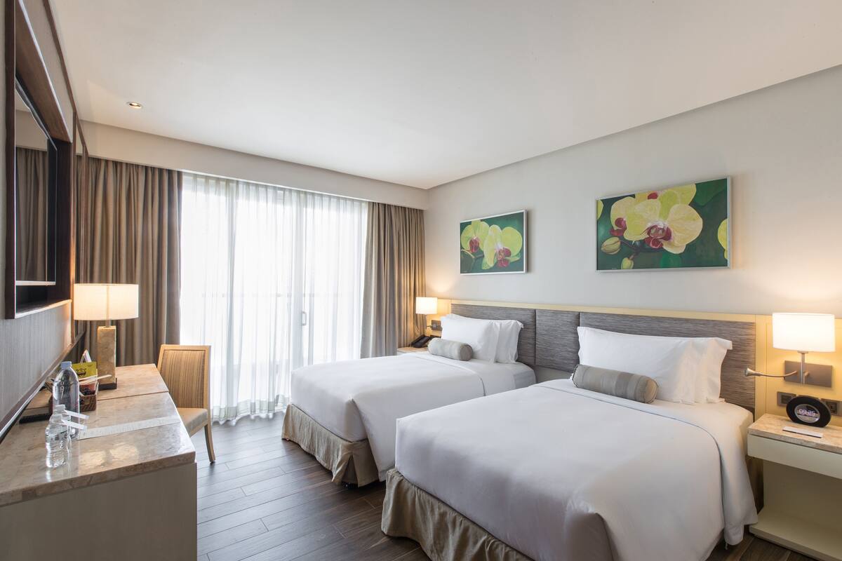 Ein Hotelzimmer mit zwei Betten, einem Schreibtisch, einer Lampe und einem Bild an der Wand.