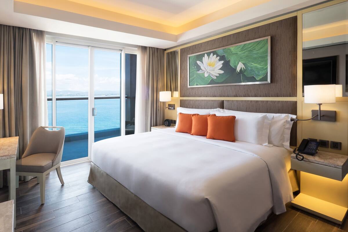 Ein Hotelzimmer mit einem großen Bett, einem Schreibtisch, einem Stuhl und Meerblick durch eine Schiebetür.