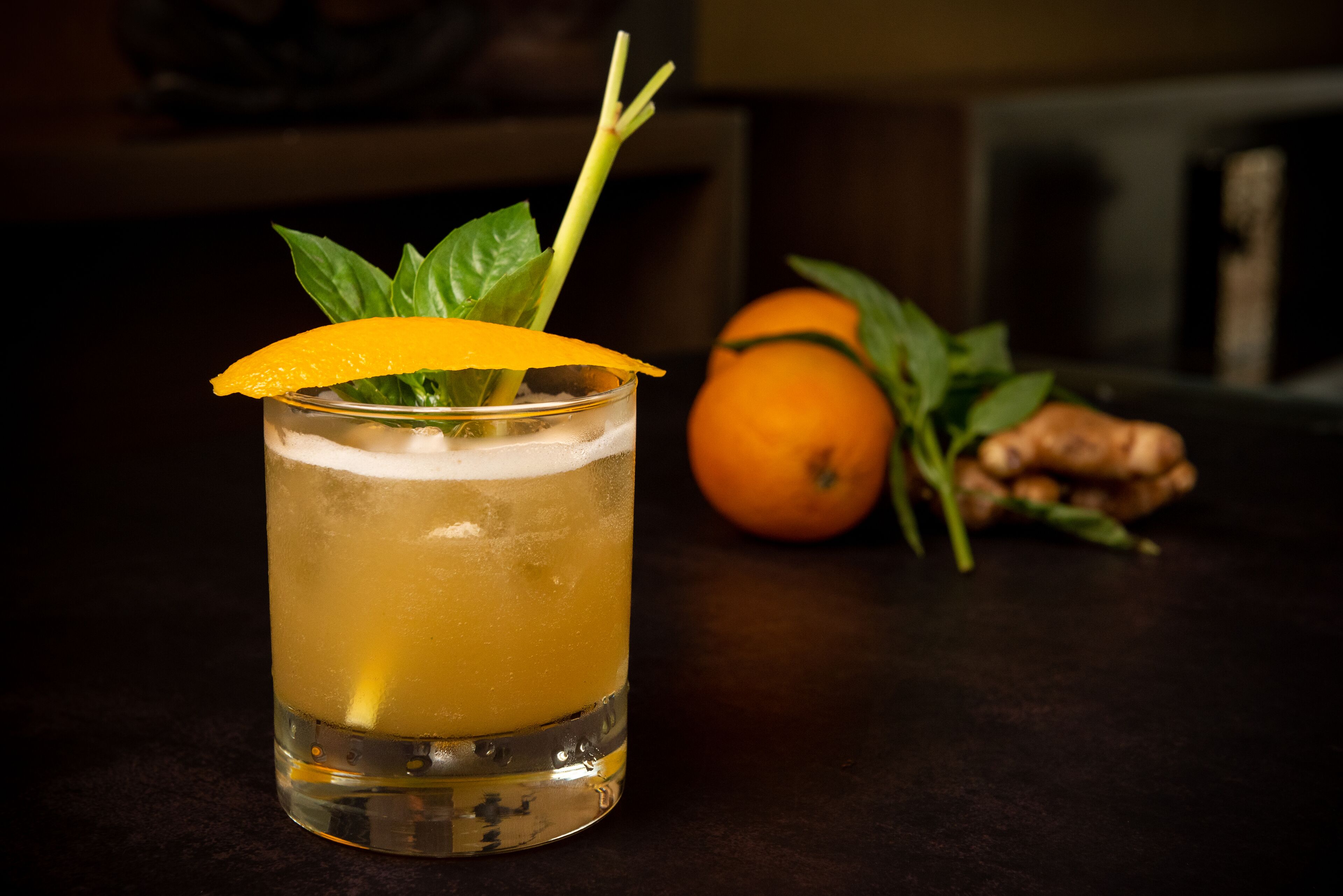 A glass of amber-colored beverage with a lemon slice garnish, placed on a dark surface.