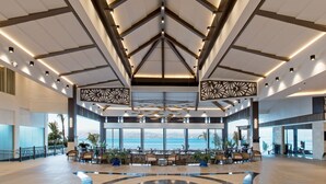 Un hall espacioso con un techo alto, grandes ventanales que ofrecen vistas al mar y un área de estar con mesas y sillas.