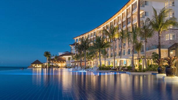 Un hotel con piscina, palmeras y vista al mar.