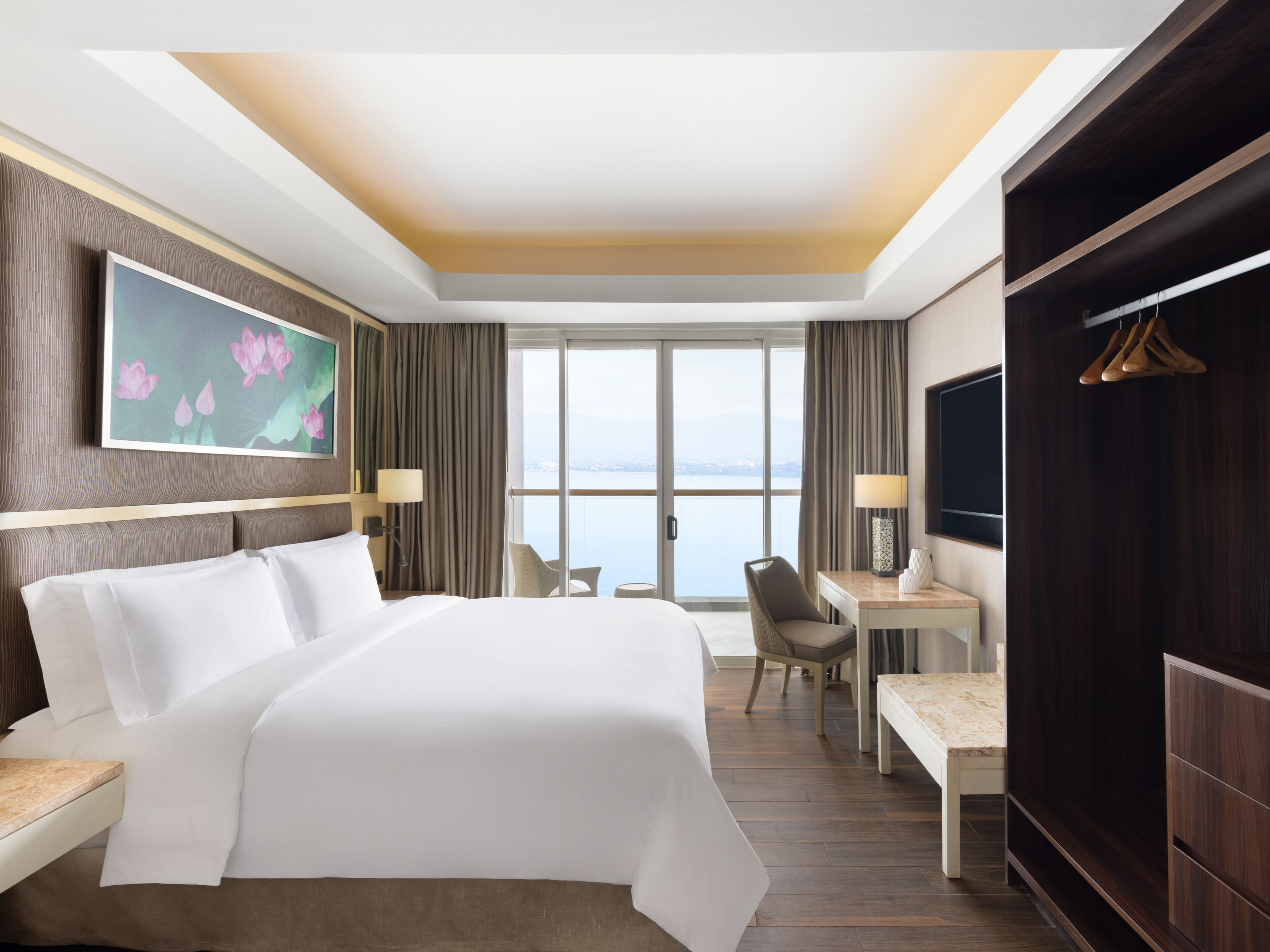 A hotel room with a large bed, a desk, a chair, a TV, and a view of the water.