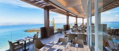 An outdoor dining area with tables and chairs, overlooking a body of water.