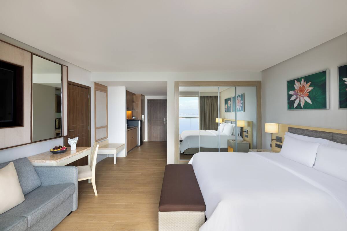 Ein Hotelzimmer mit einem großen Bett, einer Sitzecke, einem Schreibtisch mit Computer und Blick auf die Stadt.