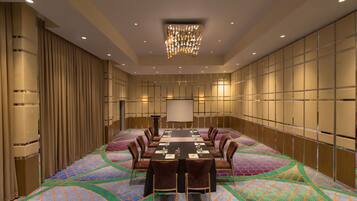 A conference room with a long table, chairs, a projector screen, and a patterned carpet.