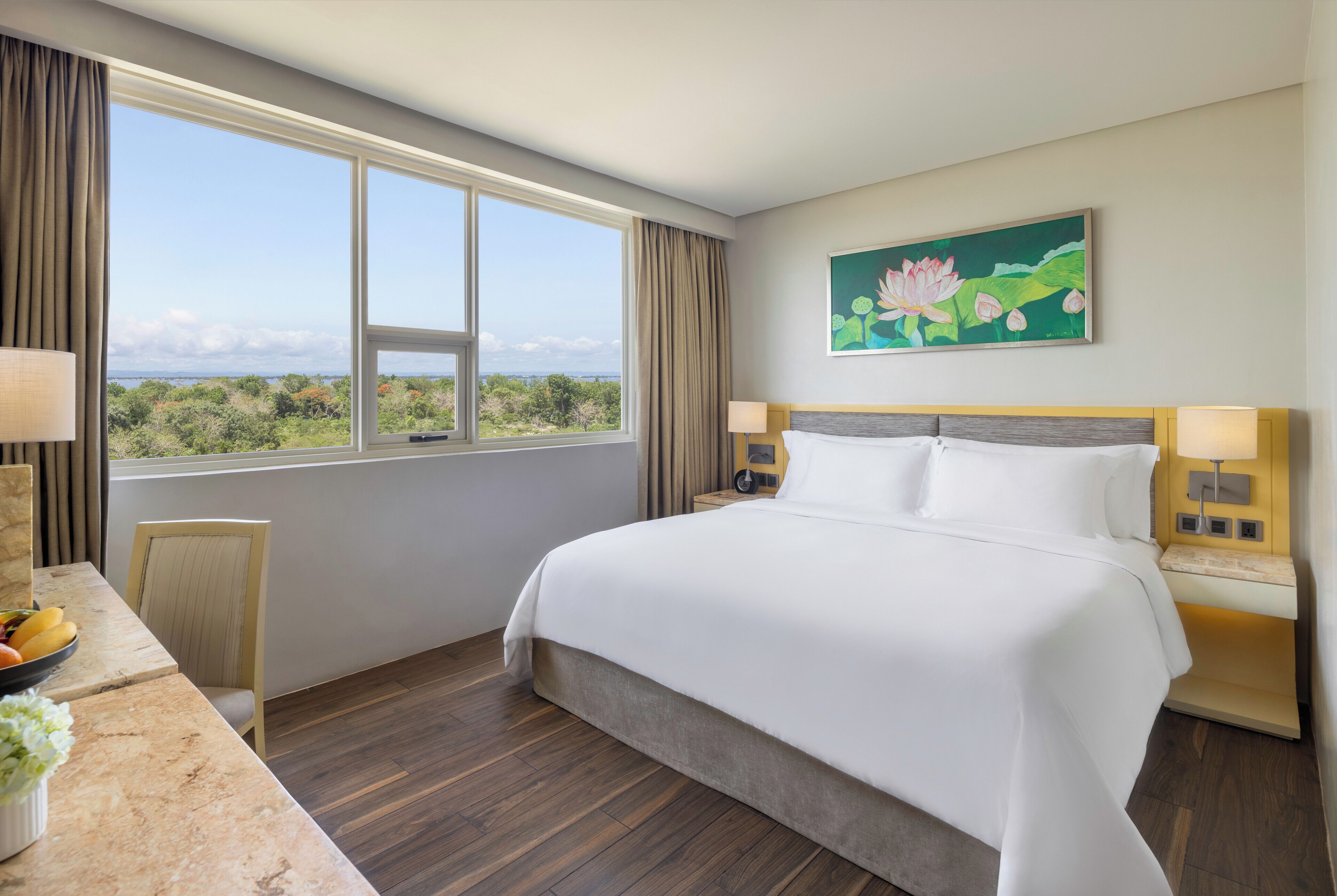A hotel room with a large bed, a desk with a lamp, a chair, and a view of the outdoors.